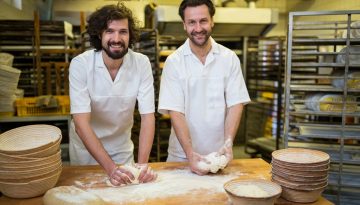 Two smiling bakers kneading dough on the counter